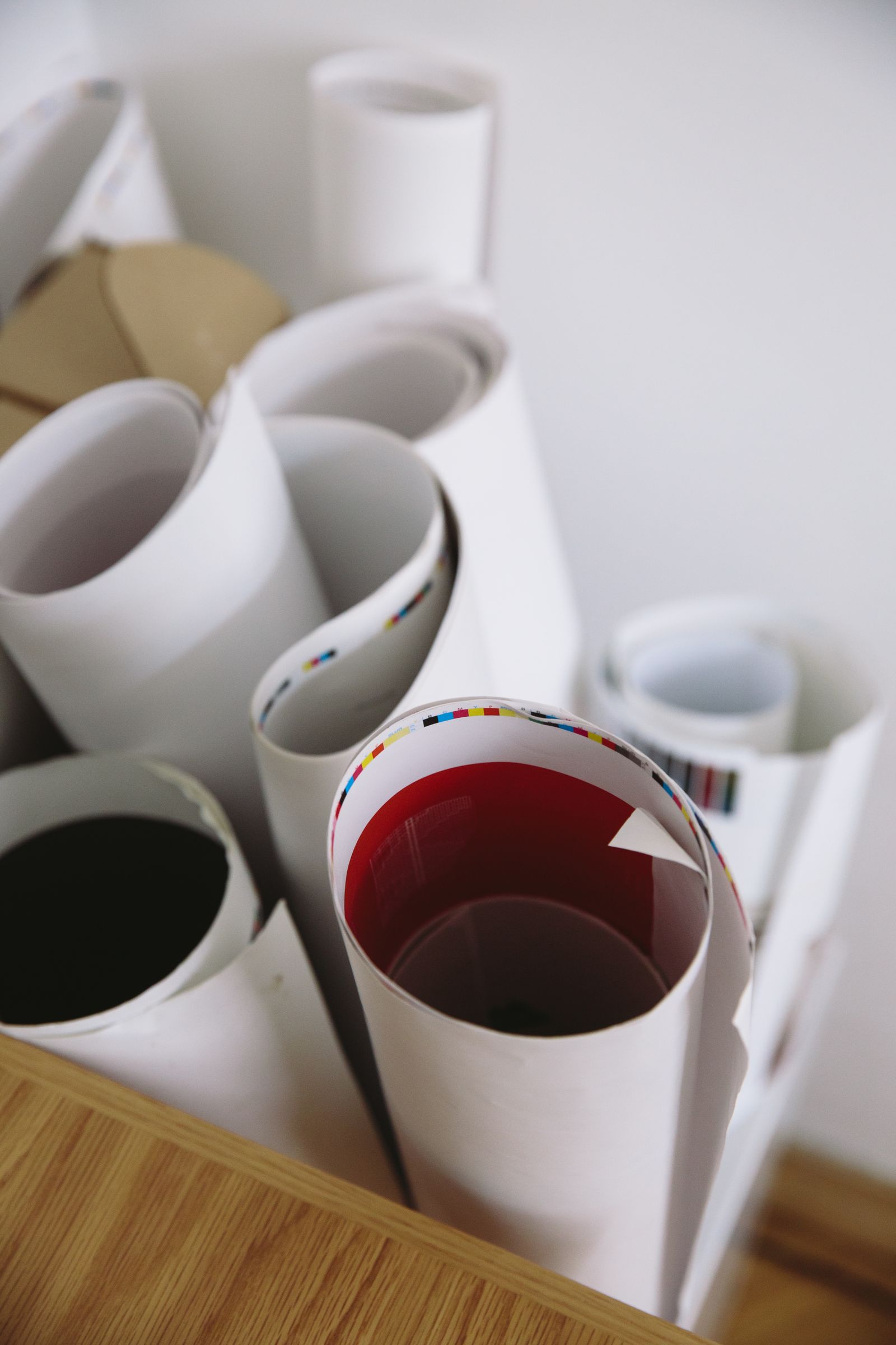 A cluster of rolled-up large-format prints and posters standing on end on a wooden surface, their cut edges showing CMYK colour-registration bars.